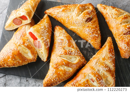 Puff pastry turnover with sausage, cheese and pepper close-up on a marble board. Horizontal top view Puff pastry turnover with sausage, cheese and pepper close-up on a marble board. Horizontal top view 112220273