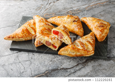 Delicious puff pastry pies with sausage, cheese, sesame and pepper close-up on a marble board. Horizontal 112220281
