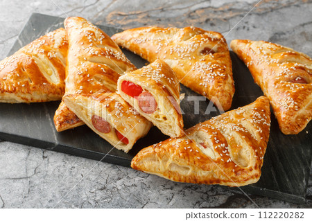 Puff pastry Pigs in a blanket pies with sausage, cheese, sesame and pepper close-up on a marble board. Horizontal Puff pastry Pigs in a blanket pies with sausage, cheese, sesame and pepper close-up on a marble board. Horizontal 112220282