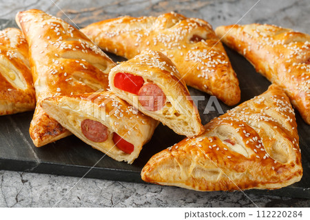 Puff pastry turnover with sausage, cheese and pepper close-up on a marble board. Horizontal Puff pastry turnover with sausage, cheese and pepper close-up on a marble board. Horizontal 112220284
