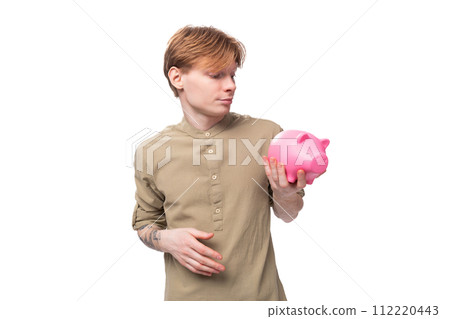young handsome redhead student man holding piggy bank with savings young handsome redhead student man holding piggy bank with savings 112220443