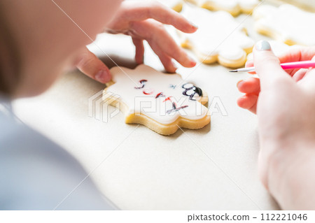 A heartwarming scene of a little girl carefully writing 'Sorry' on sugar cookies with food coloring, the cookies beautifully flooded with white royal icing. A heartwarming scene of a little girl carefully writing 'Sorry' on sugar cookies with food coloring, the cookies beautifully flooded with white royal icing. 112221046