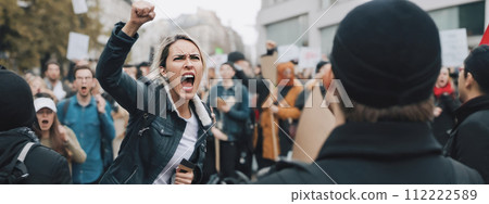 Woman passionately yelling during protest, surrounded by crowd of demonstrators on city streets, expressing strong emotions 112222589