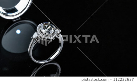 Elegant white gold ring adorned with sparkling diamonds, showcased on reflective black surface that highlights brilliance and intricate design, perfect for engagements or special occasions. 112222657
