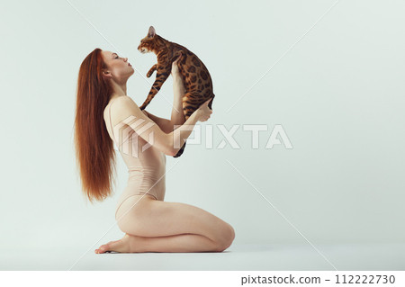 Bond between human and pet. Beautiful young redhead woman with Bengal cat against white studio background 112222730