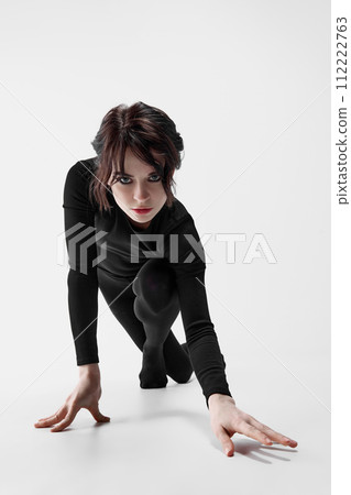 Elegant, passionate woman with dark eyes makeup, black clothes walking slowly like cat against white studio background Elegant, passionate woman with dark eyes makeup, black clothes walking slowly like cat against white studio background 112222763