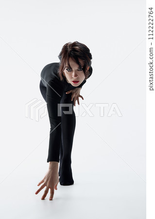 Elegant, passionate woman with dark eyes makeup, black clothes walking slowly like cat against white studio background 112222764