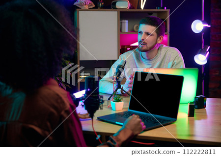 Young people, social media influencers sitting at table with microphones and laptops, recording podcast, interview, discussing topics Young people, social media influencers sitting at table with microphones and laptops, recording podcast, interview, discussing topics 112222811