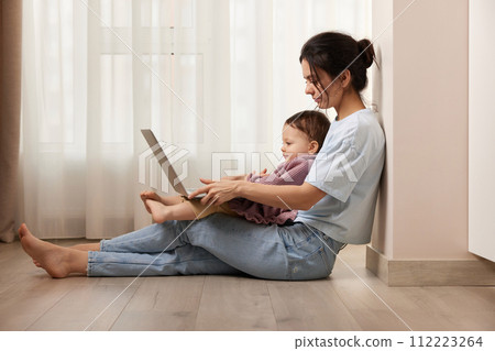 beautiful casual woman sitting on the floor and working on laptop with her little child girl at home beautiful casual woman sitting on the floor and working on laptop with her little child girl at home 112223264