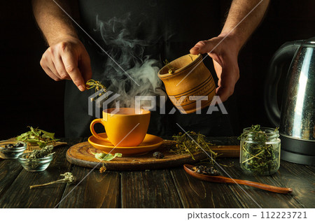A man adds dry chamomile to a mug of boiling water to make medicinal tea for a cold. Traditional medicine concept or making healthy aromatic tea 112223721