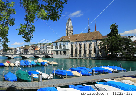 View of the clear summer sky, Münster Bridge, Wasser Church and boats from the pier on the Limmat River (Zurich, Switzerland) 112224132