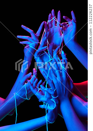 Hands interact with luminescent threads in multicolored neon lighting against black studio background, symbolizing connectivity and complexity. Hands interact with luminescent threads in multicolored neon lighting against black studio background, symbolizing connectivity and complexity. 112226237