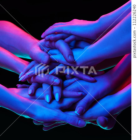 Various woman puts his hands together showcasing unity, teamwork and support in multicolored neon lighting against black studio background. Various woman puts his hands together showcasing unity, teamwork and support in multicolored neon lighting against black studio background. 112226240