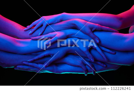 Overlapping hands in multicolored neon lighting against black studio background, suggesting unity. 112226241