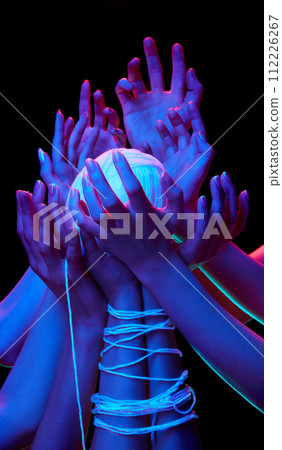 Hands encircle glowing ball of threads in multicolored neon lighting against black studio background, symbolizing global unity. 112226267