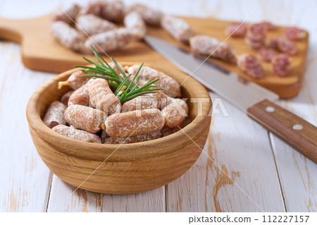 Mini salami sausages in a bowl on a white wooden table. Mini salami sausages in a bowl on a white wooden table. 112227157