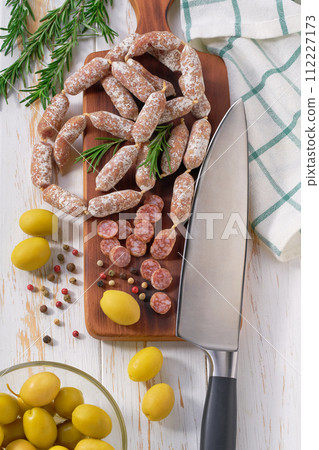 Mini salami sausages with rosemary and olives on a wooden cutting board, top view. 112227173