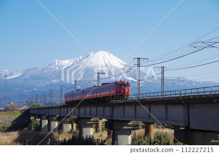 Rear view of a Kiha 40 series Kiha 47 regular train (4-car train) passing the Hino River railway bridge with snow-capped Mt. Daisen in the background. 112227215