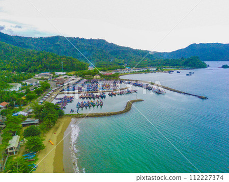A vibrant aerial view of Prigi Beach in East Java, Indonesia. Dozens of colorful fishing boats bob gently in the turquoise waters. A vibrant aerial view of Prigi Beach in East Java, Indonesia. Dozens of colorful fishing boats bob gently in the turquoise waters. 112227374