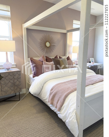 This inviting bedroom features an elegant white canopy bed adorned with soft pink and taupe pillows, creating a serene and cozy atmosphere. The warm lighting from the bedside lamps casts a soothing This inviting bedroom features an elegant white canopy bed adorned with soft pink and taupe pillows, creating a serene and cozy atmosphere. The warm lighting from the bedside lamps casts a soothing 112227855