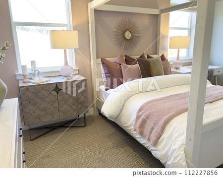 This inviting bedroom features an elegant white canopy bed adorned with soft pink and taupe pillows, creating a serene and cozy atmosphere. The warm lighting from the bedside lamps casts a soothing This inviting bedroom features an elegant white canopy bed adorned with soft pink and taupe pillows, creating a serene and cozy atmosphere. The warm lighting from the bedside lamps casts a soothing 112227856