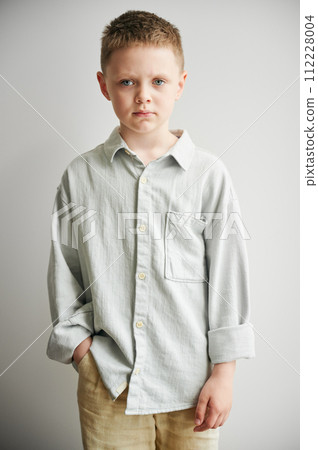 Portrait of young sad boy keeping hand in pocket, looking to the camera. Serious kid in casual clothes posing on white background. 112228004