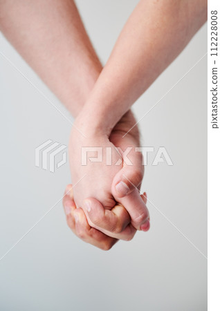 Two hands held together in grasp against neutral background. Close up of man's and woman's hand. Concept of intimacy, support, and trust. 112228008
