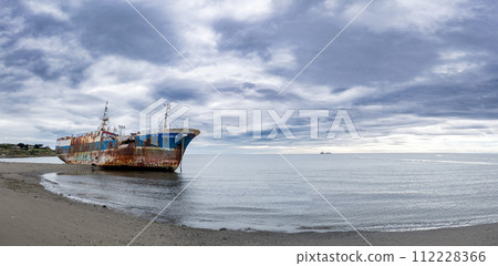 Rusted Shipwreck on Serene Beach Under Cloudy Sky 112228366