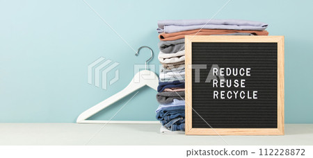 Black letter box and stack of folded clothes on blue background, reduce,reuse,recycle quote 112228872