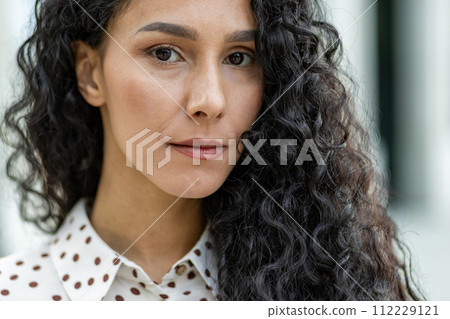 Close-up of an elegant curly-haired woman in a stylish polka-dot blouse. The image captures a fashionable female detail, perfect for beauty and fashion themes. Close-up of an elegant curly-haired woman in a stylish polka-dot blouse. The image captures a fashionable female detail, perfect for beauty and fashion themes. 112229121