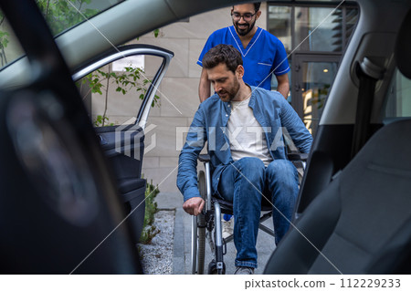 Disabled man getting on a car, male nurse helping him Disabled man getting on a car, male nurse helping him 112229233