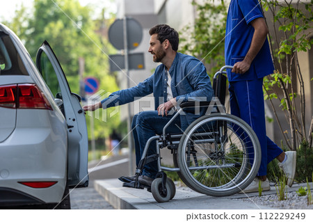 Dark-haired man on a wheelchair opening a car door Dark-haired man on a wheelchair opening a car door 112229249