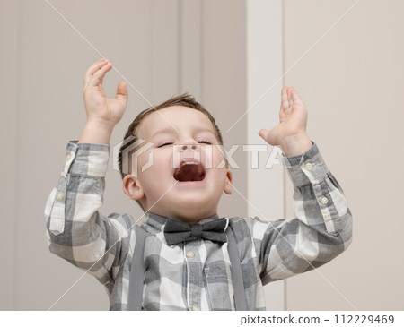 Emotions of happiness, fun, joy and delight on the child s face. A small handsome boy of 4 years old in a shirt with a bow tie shows a mime with a facial expression. 112229469