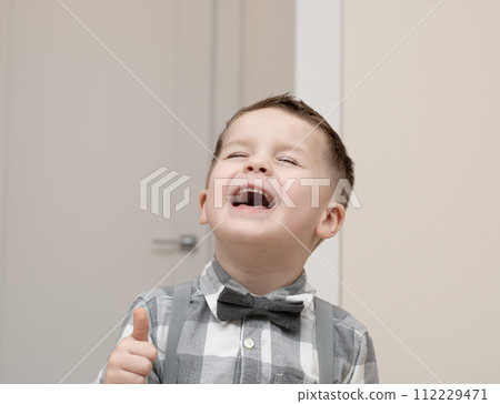 Emotions of happiness, fun, joy and delight on the child s face. A small handsome boy of 4 years old in a shirt with a bow tie shows a mime with a facial expression. Emotions of happiness, fun, joy and delight on the child s face. A small handsome boy of 4 years old in a shirt with a bow tie shows a mime with a facial expression. 112229471
