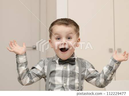 Emotions of surprise and delight on the child s face. A small handsome boy of 4 years old in a shirt with a bow tie shows a grimace with an expression on his face. Close-up. Emotions of surprise and delight on the child s face. A small handsome boy of 4 years old in a shirt with a bow tie shows a grimace with an expression on his face. Close-up. 112229477