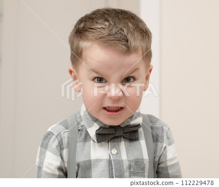 Emotions of anger and anger on a child's face. A small handsome boy, 4 years old, wearing a shirt with a bow tie, shows a grimace with facial expressions. Emotions of anger and anger on a child's face. A small handsome boy, 4 years old, wearing a shirt with a bow tie, shows a grimace with facial expressions. 112229478