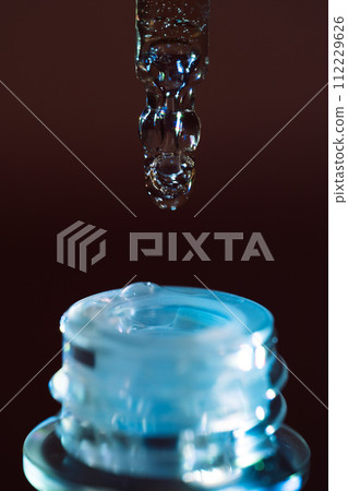 A drop of serum flows from a pipette into a jar under blue light A drop of serum flows from a pipette into a jar under blue light 112229626