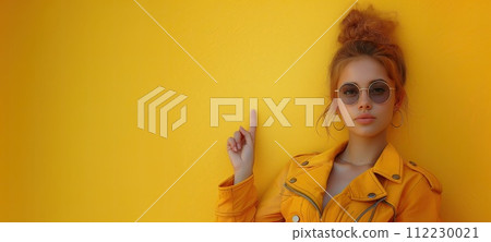 Portrait of a beautiful girl in a yellow jacket and sunglasses on a yellow background. Banner, copy space 112230021