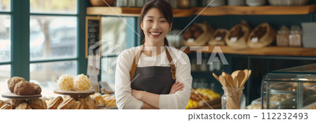 Asian woman wearing an apron with arms crossed inside a bakery shop. 112232493