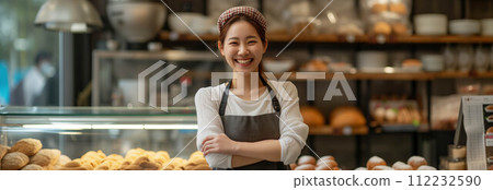 Asian woman wearing an apron with arms crossed inside a bakery shop. Asian woman wearing an apron with arms crossed inside a bakery shop. 112232590