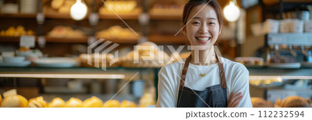 Asian woman wearing an apron with arms crossed inside a bakery shop. 112232594