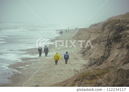 People walk on the beach in stormy weather in Sondervig Denmark 112234117