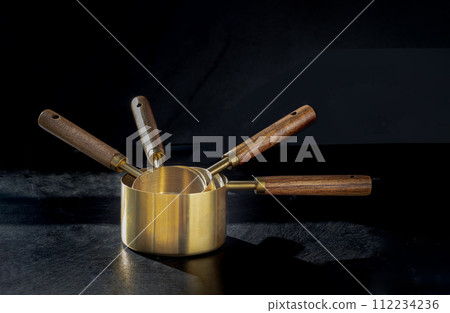 Set of Brass Measuring Cups with Wood Handles with Hanging Hole Design on dark background. 112234236