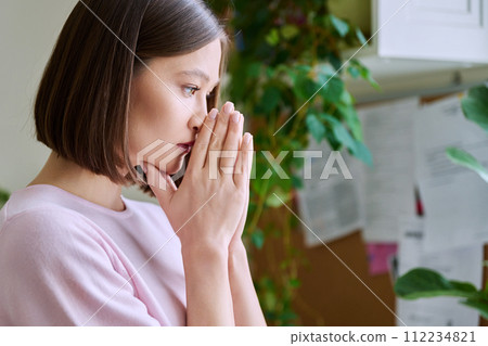 Profile view close-up of young woman's face with hands folded in prayer, dreams Profile view close-up of young woman's face with hands folded in prayer, dreams 112234821