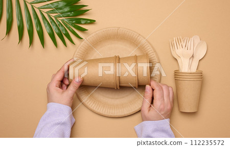 Paper plates and cups, wooden spoons and forks on a beige background, top view Paper plates and cups, wooden spoons and forks on a beige background, top view 112235572