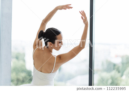 Female ballet dancer makes pirouette at ballet studio in front of big window. 112235995