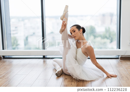 Beautiful ballerina sitting at wooden studio floor and stretching. Beautiful ballerina sitting at wooden studio floor and stretching. 112236228