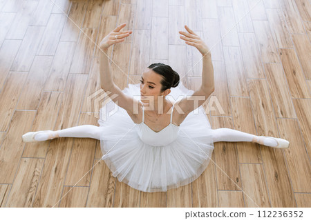 Professional ballerina in tutu and pointe stretching on floor. 112236352
