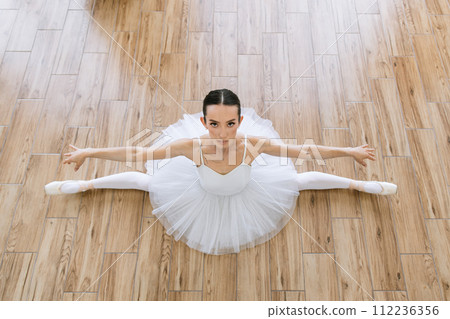 Young woman ballerina in white pack posing on background of wooden floor. 112236356