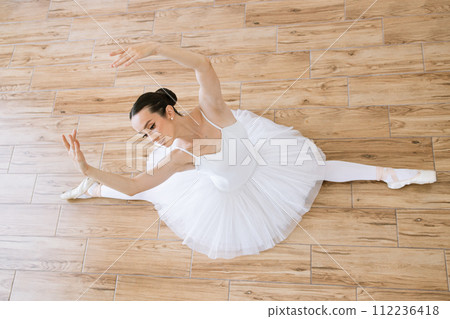 Top view of professional caucasian ballerina in white tutu and pointe stretching Top view of professional caucasian ballerina in white tutu and pointe stretching 112236418